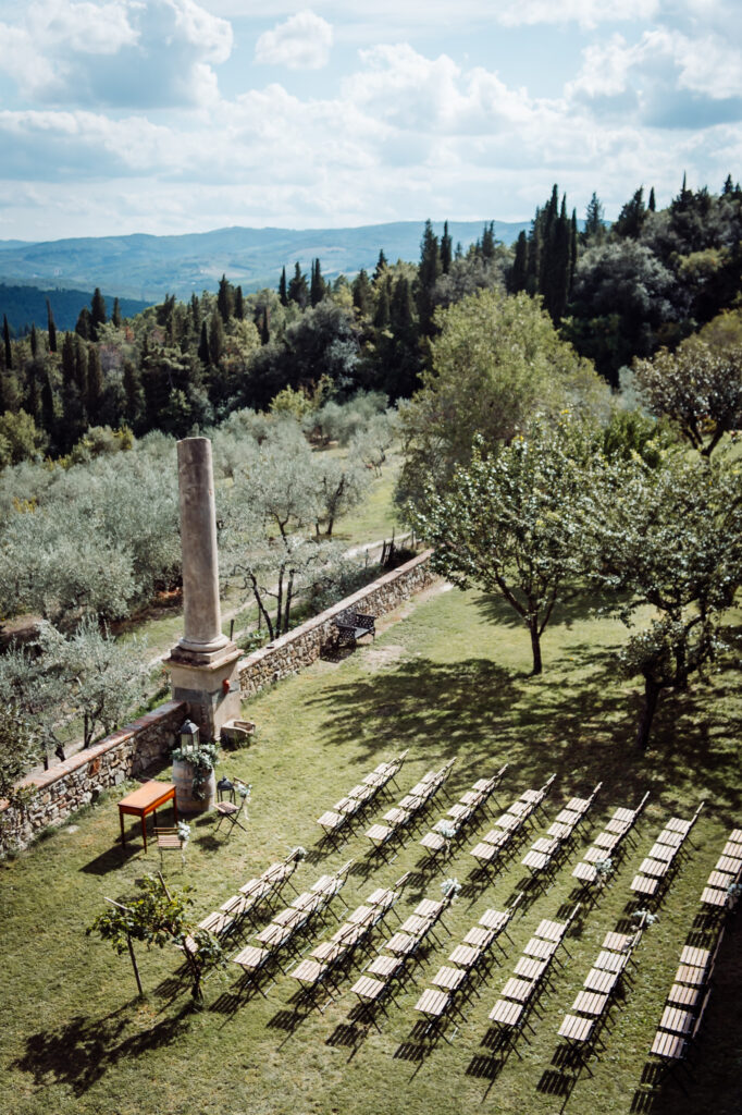 Outdoor wedding ceremony setup overlooking Tuscan hills at Castello di Cafaggio, surrounded by olive trees and cypress forests.