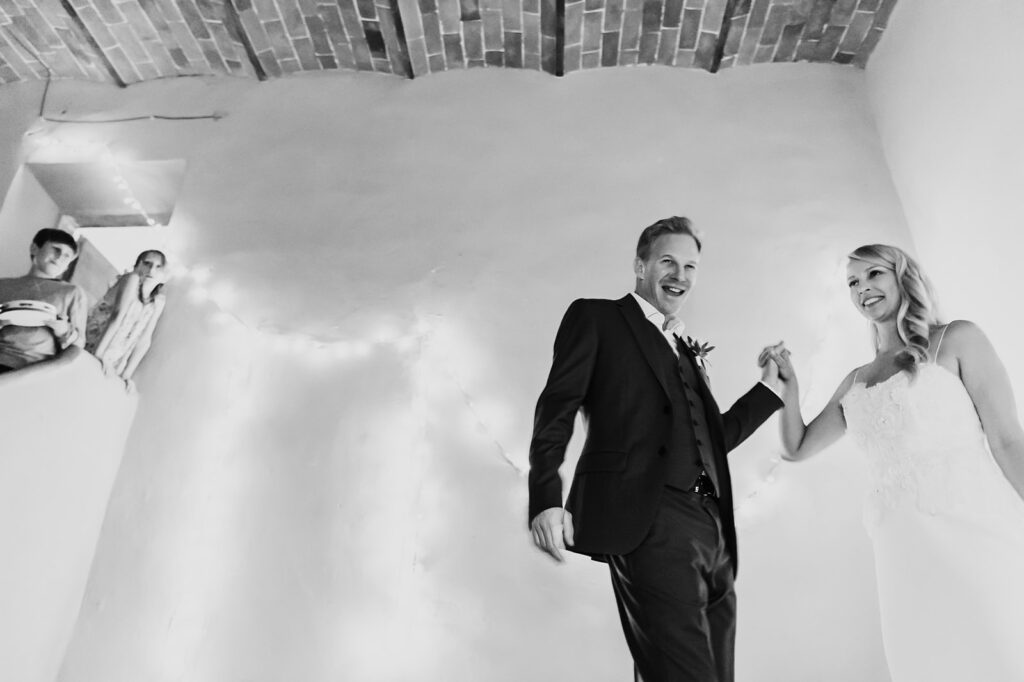 A candid black and white photo of the bride and groom laughing and holding hands during their final celebration