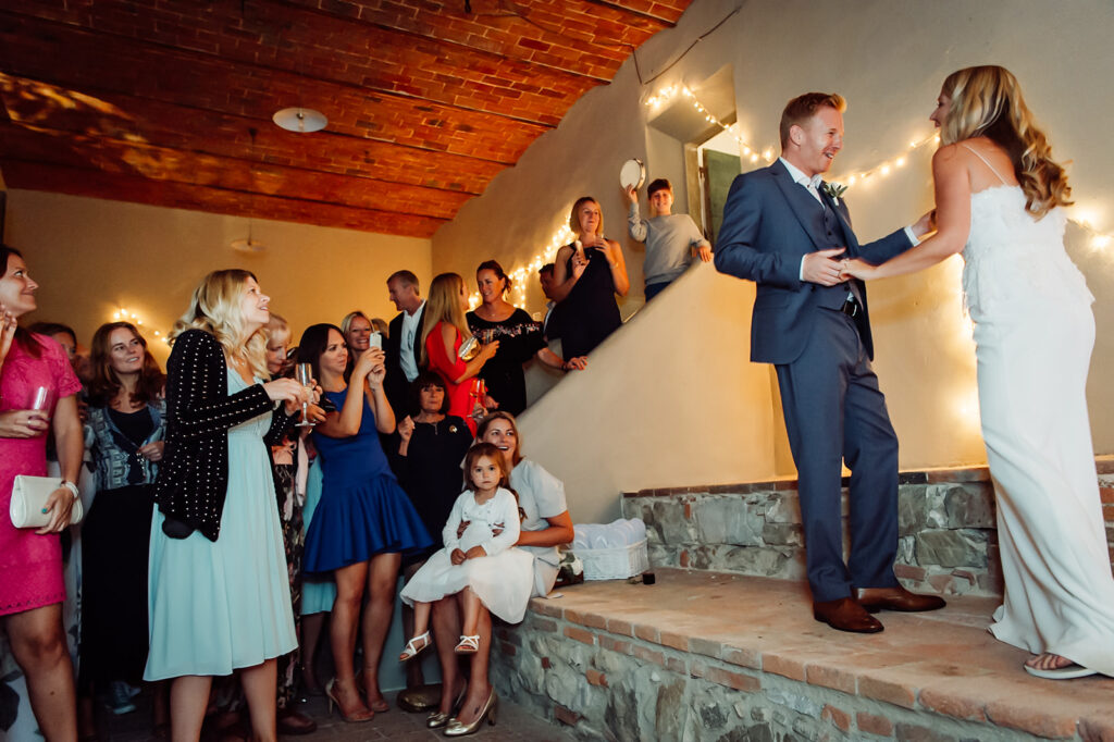 A candid wide shot of the bride and groom dancing while guests watch and smile
