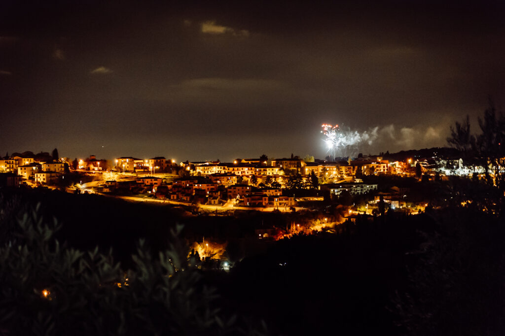 Scenic nighttime view of a Tuscan town with fireworks lighting up the sky