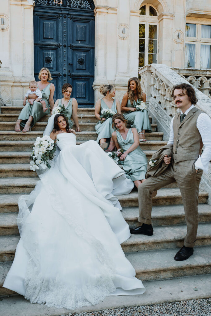 Bride, groom, and bridesmaids sitting on the venue’s stairs posing for a wedding photo.
