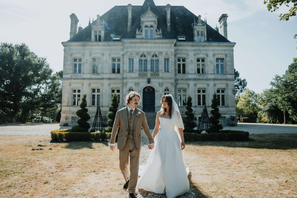 Couple holding hands in front of a beautiful stone UK wedding venue, captured by a luxury wedding photographer