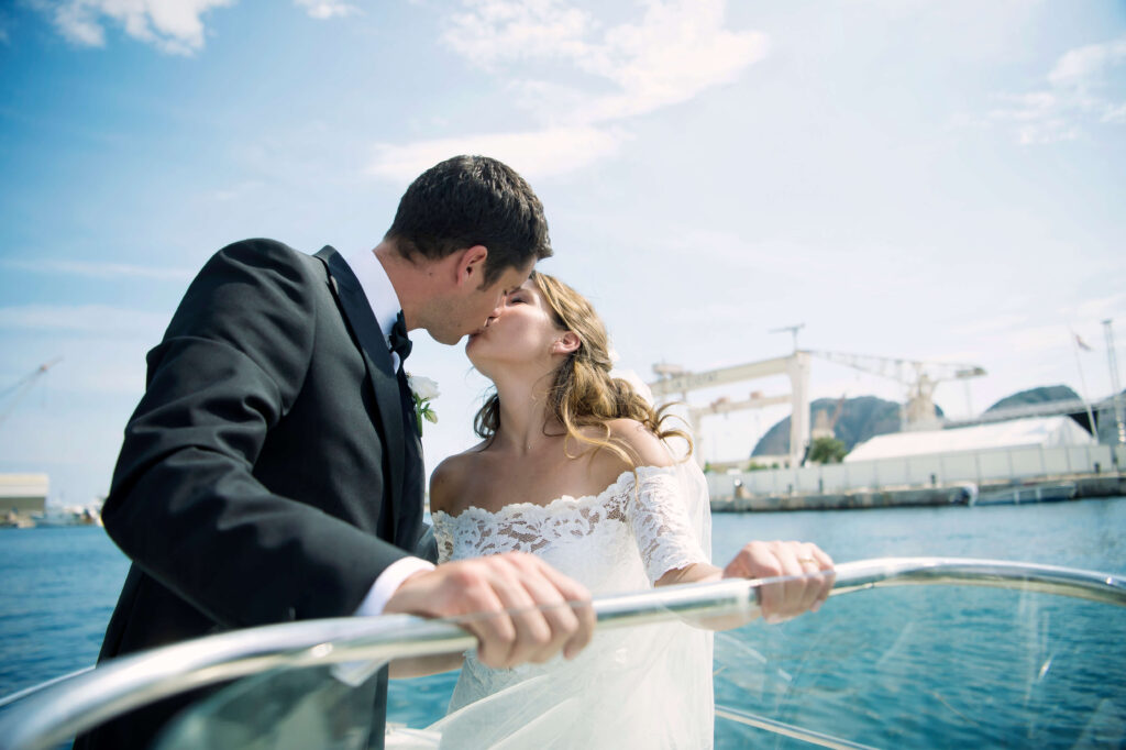 Wedding couple kissing, while holding onto the boat. sea and sky in the background