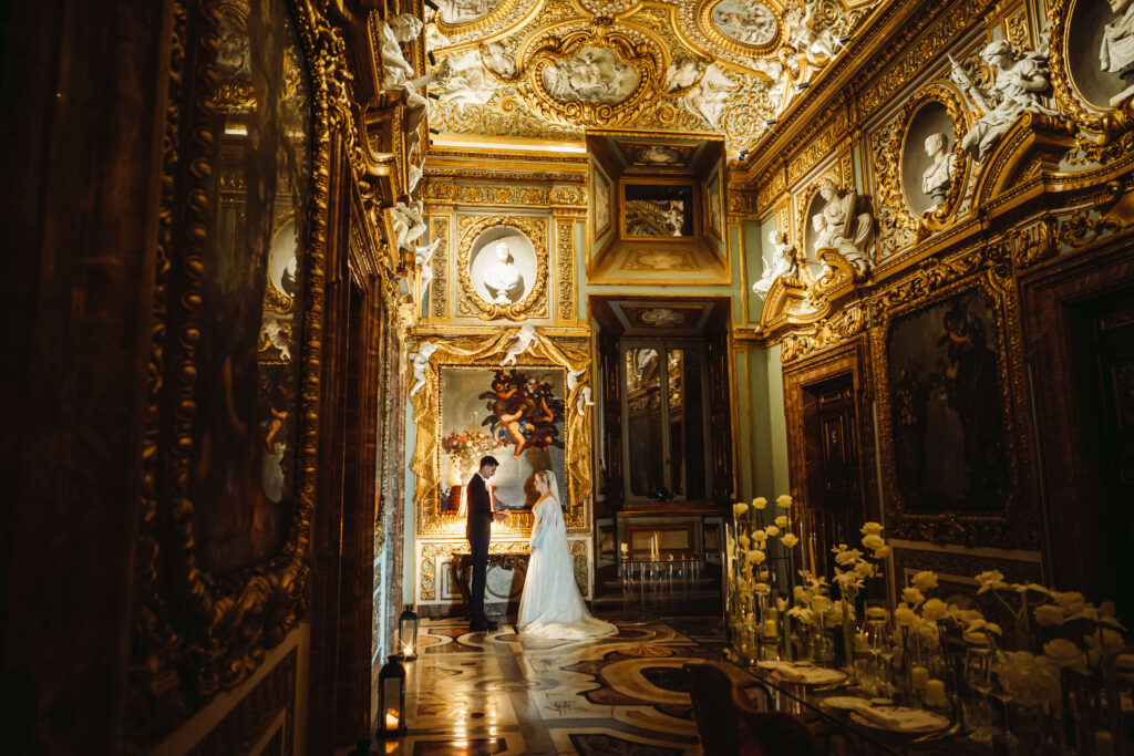 Couple looking at each other surrounded by detailed architecture. The room is Gold and white.
