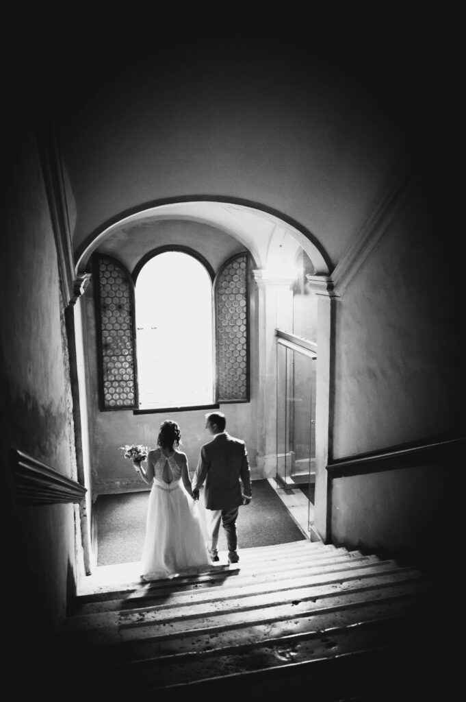 Black and white photo of wedding couple walking hand in hand down the venues stairs.