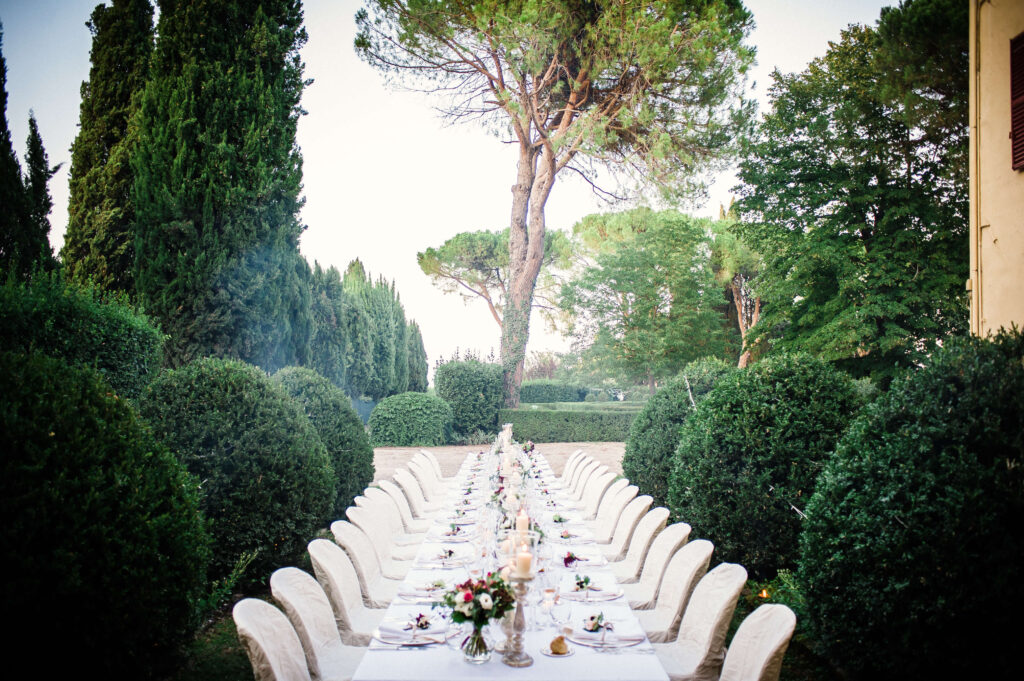 Low-angle view of a wedding table setting with candles and floral arrangements, sun-kissed trees in the background