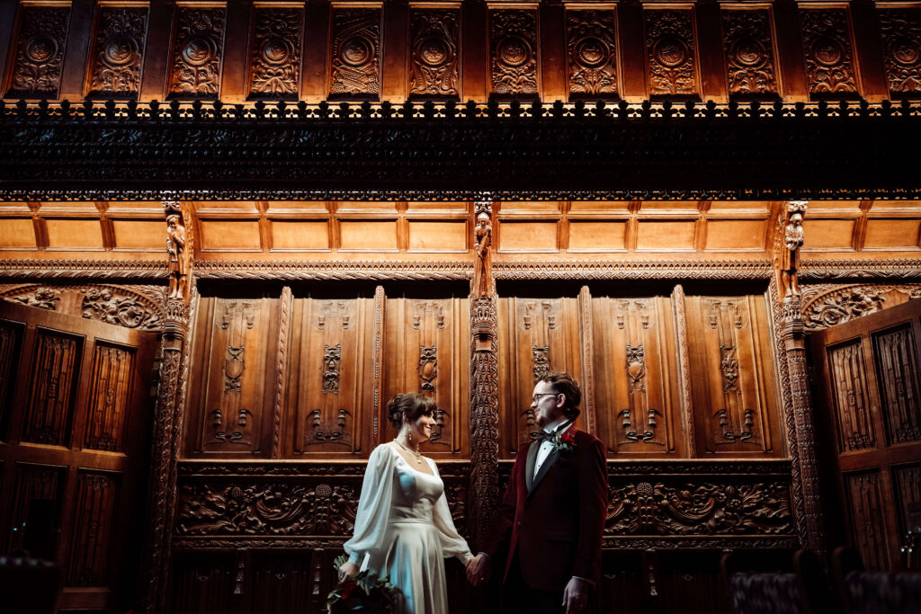 Bride and Groom looking at each other in front of an ornate carved wooden wall.