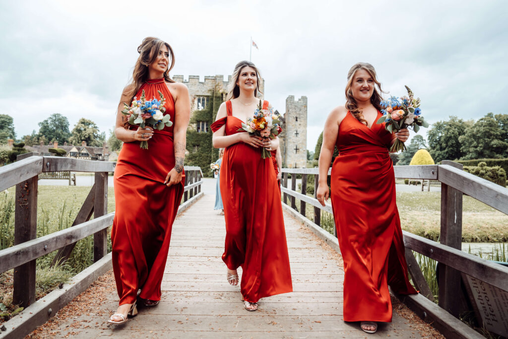 Three bridesmaids walk side by side, with Hever Castle in the background.