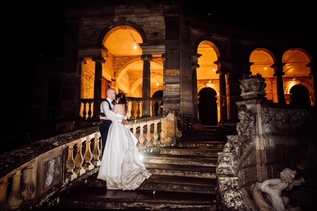Wedding couple embracing on the Loggia staircase at Hever Castle, backlit by the warm glow from the Loggia lights.