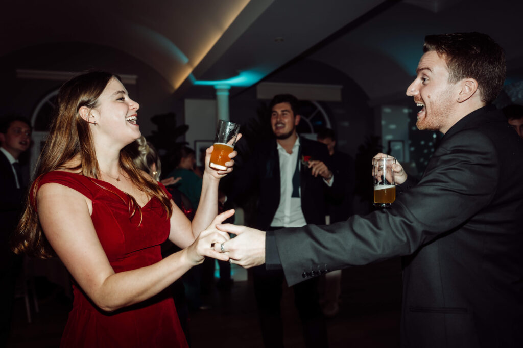 Wedding guests dancing and singing, holding drinks.