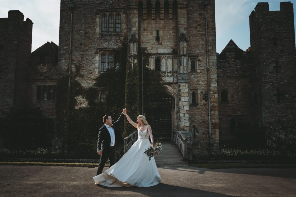 Bride twirling in her wedding dress as the groom holds her hand in front of a Hever Castle on their wedding day.