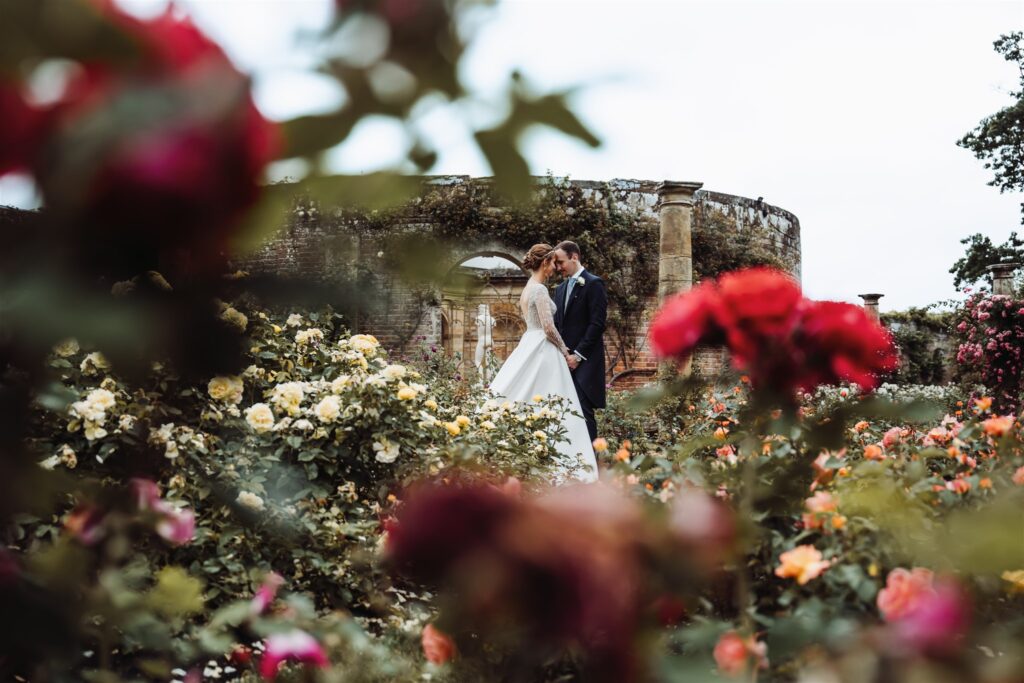 Couple embracing in Hever Castle’s rose garden, framed by blooming roses, photographed by a Hever Castle wedding photographer.