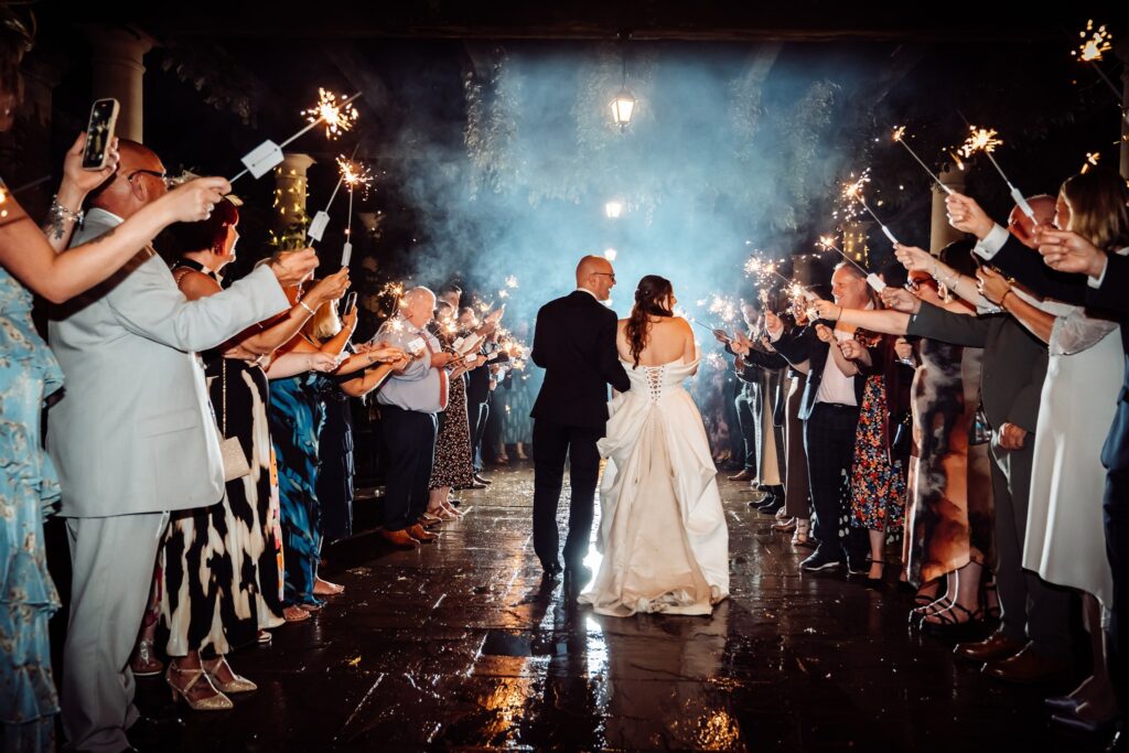 Back view of a wedding couple walking through sparklers held by their guests at Hever Castle