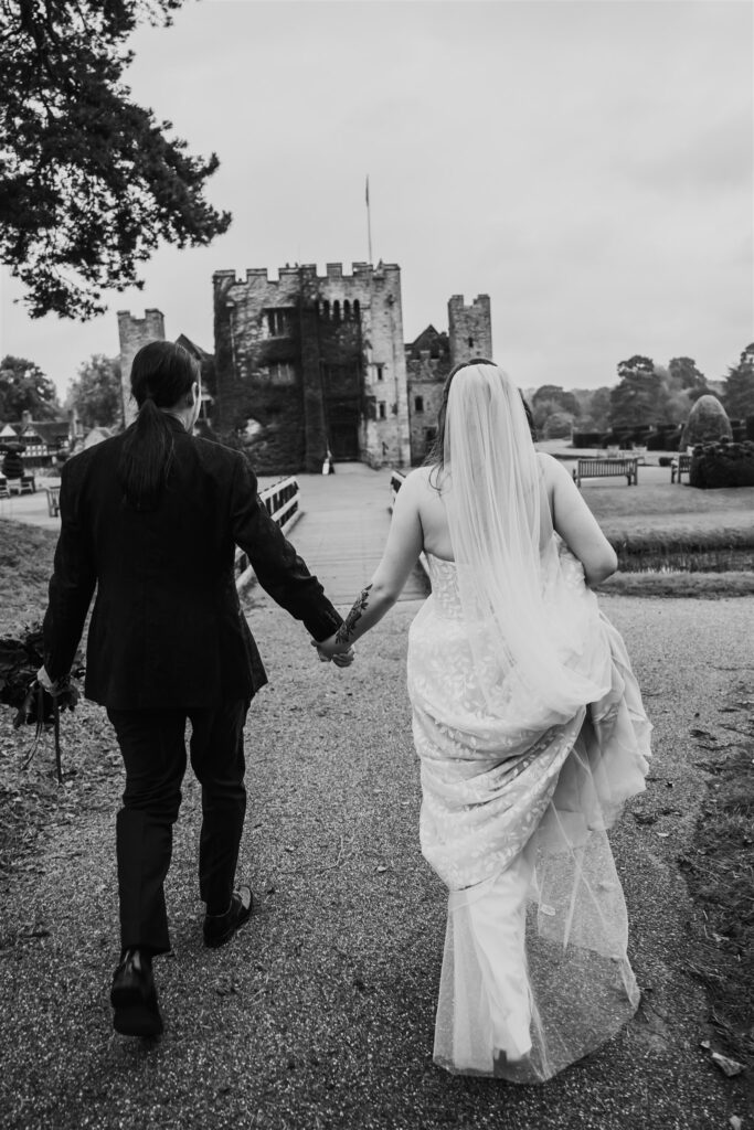 Black and white photo showing the couple from behind walking towards Hever Castle holding hands