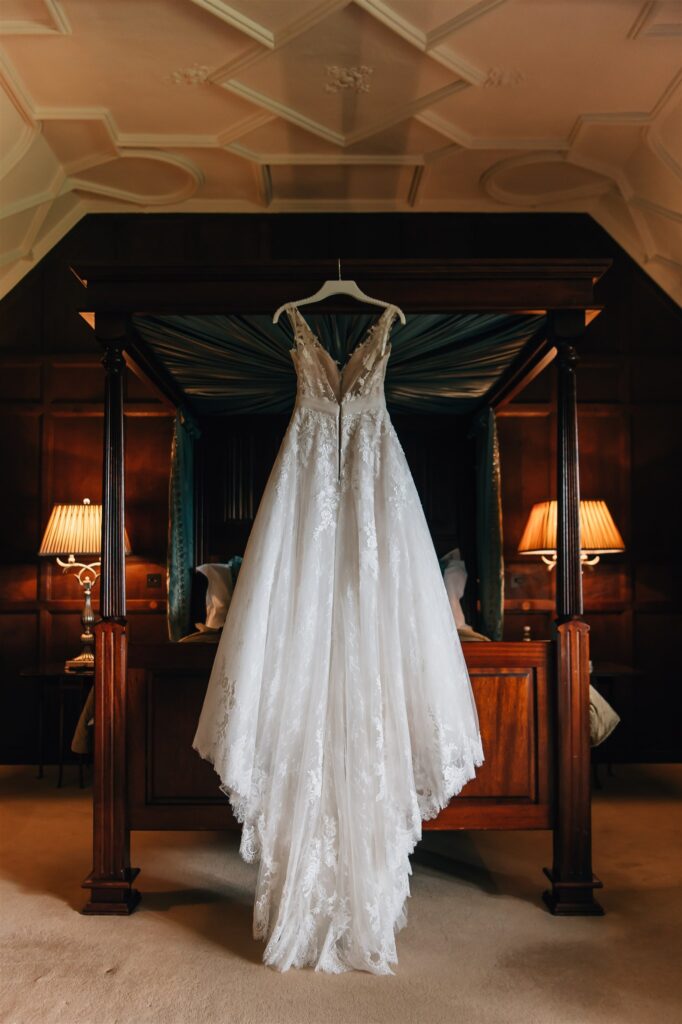 Wedding dress hung on a bed frame in Hever Castle, showcasing the bridal gown and room, captured by a Hever Castle wedding photographer